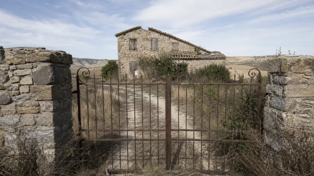 Cancello chiuso e strada bianca verso un casale in pietra da ristrutturare