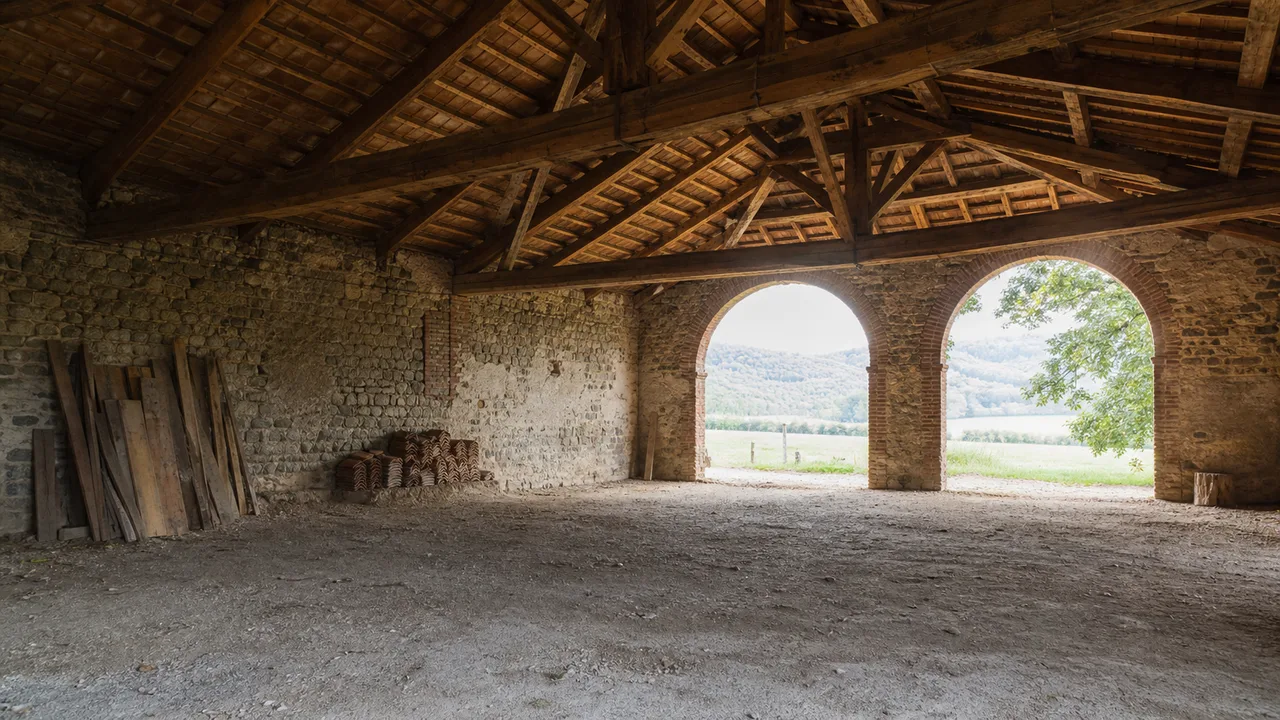 Interno di un fienile non recuperato con capriate in legno e archi aperti sulla campagna