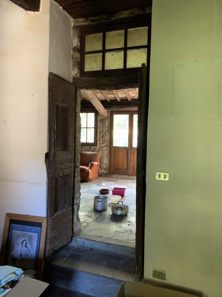 Porta in legno antico aperta su una stanza in pietra con pentole sul pavimento